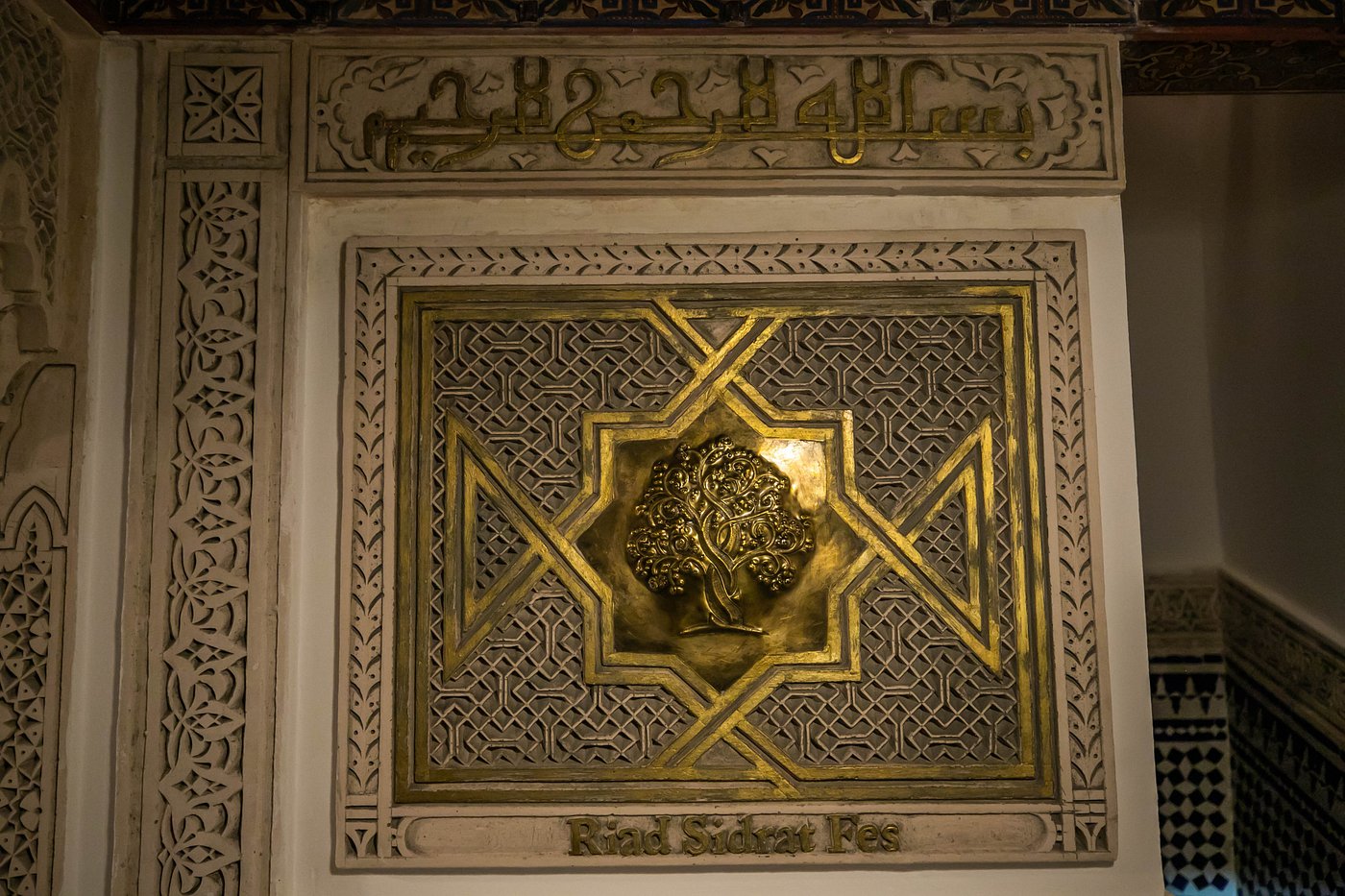 Carved wooden lintel with Arabic calligraphy above a zellige panel bearing the riad's name